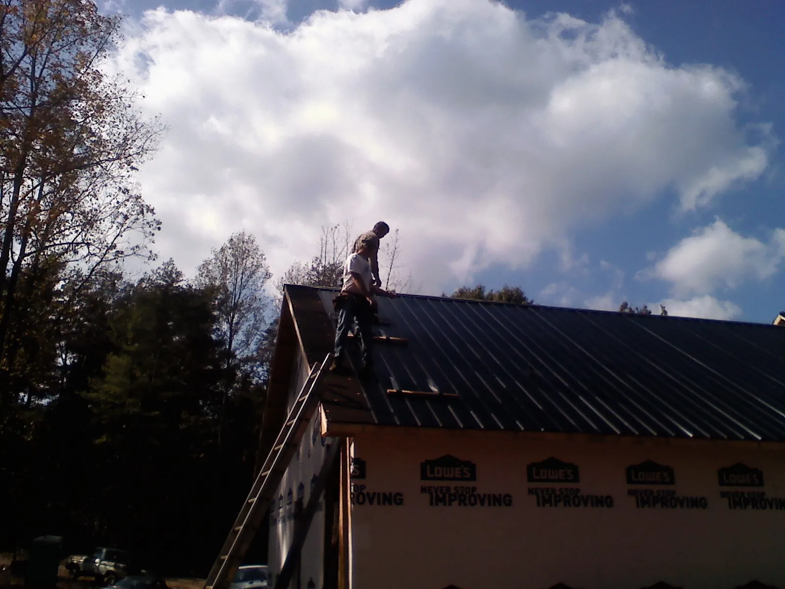 Roofer fastening dark metal panels high against a cloudy sky, from a Roof Inspection job in Alpine